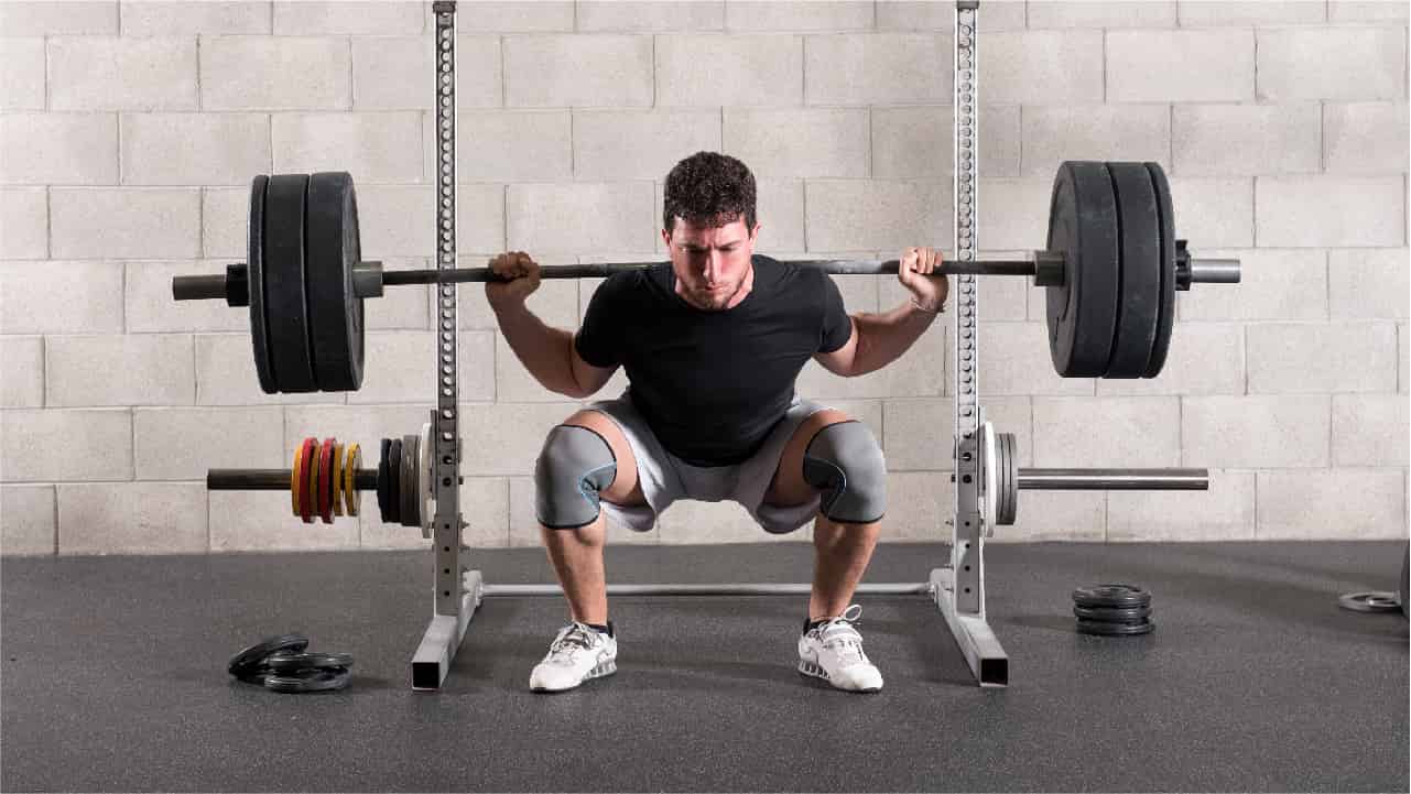Man squatting underneath a weight rack ready to lift a heavy barbell