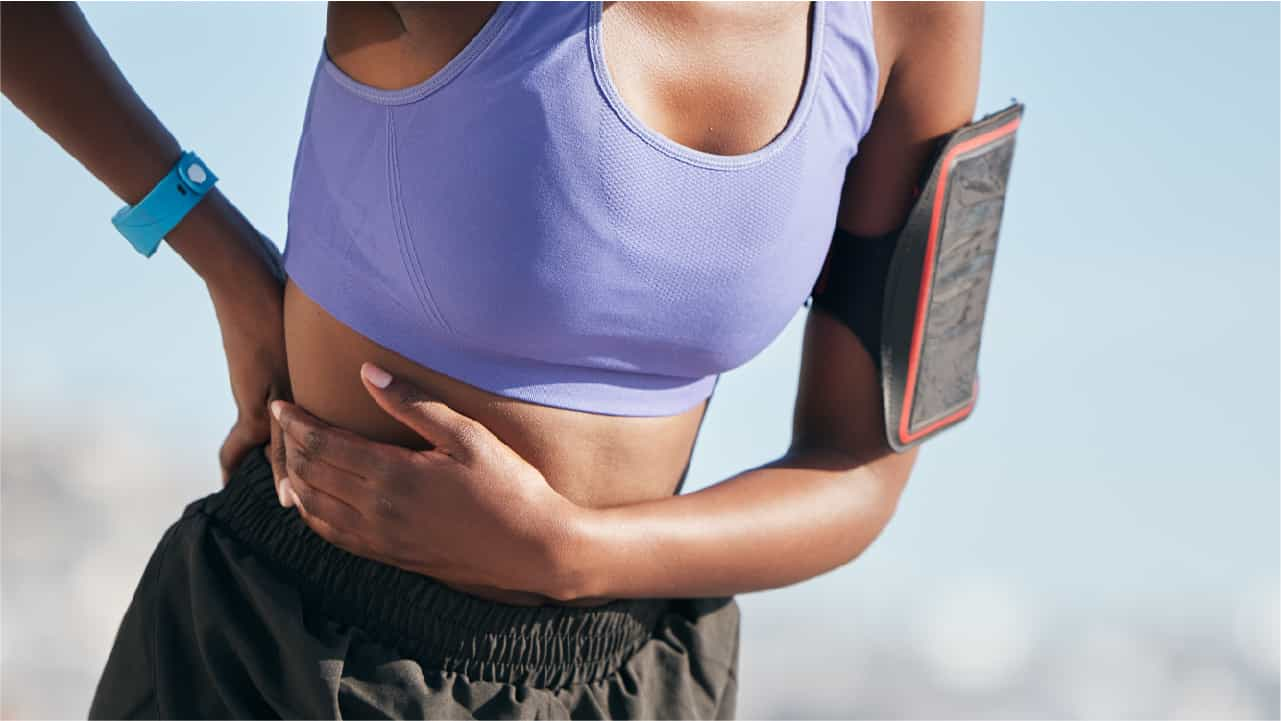 Woman in running gear holding her side. Image suggests she has a pain caused by exercise on a full stomach