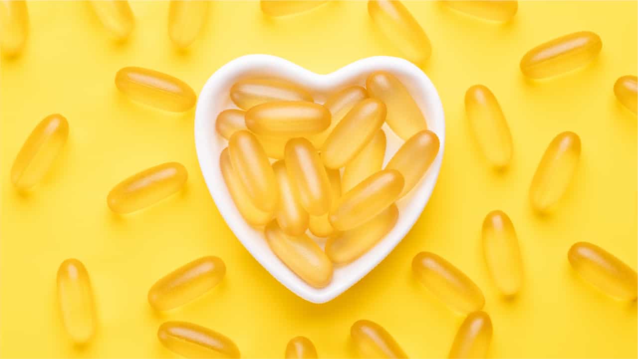 Omega 3 fish oil capsules in a heart-shaped plate on yellow background. 'Fish oil ' softgels