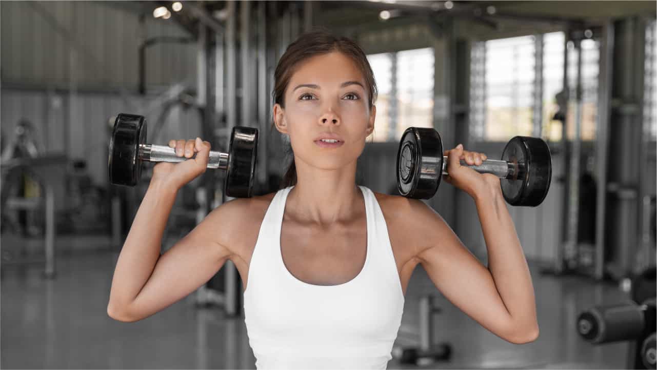 A female in the gym performing a dumbbell shoulder press, demonstrating how to get lean arms