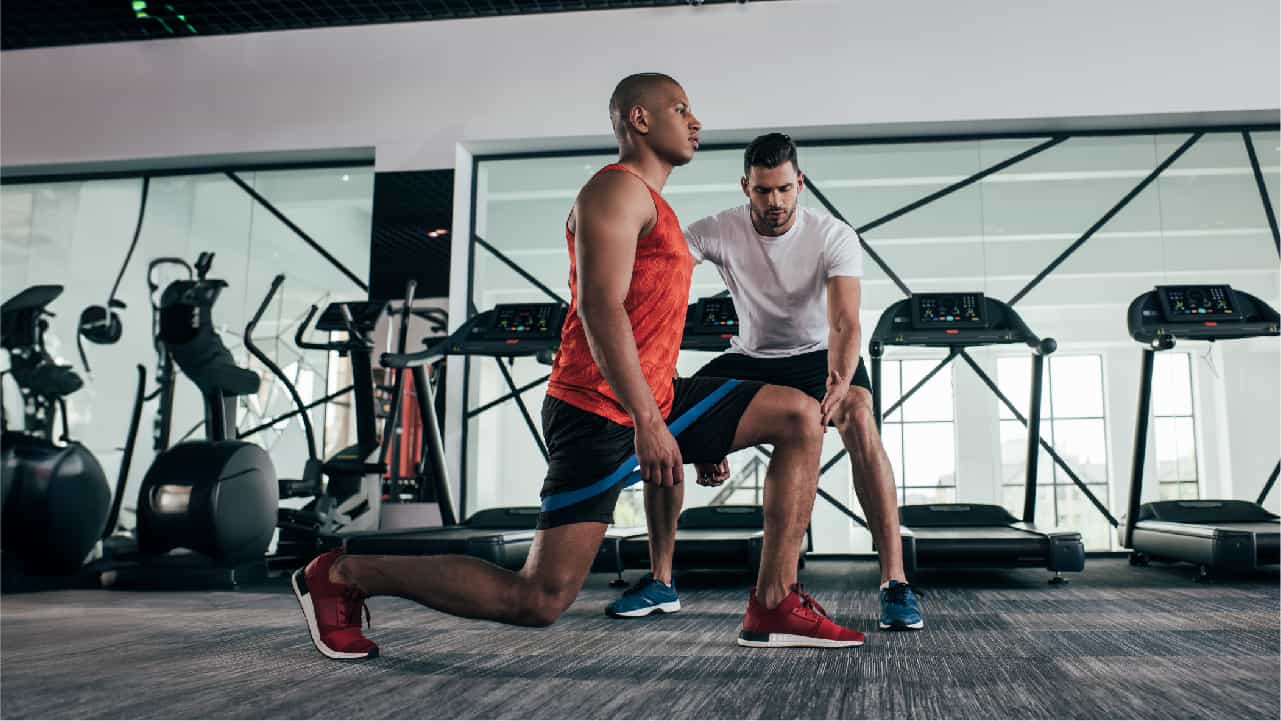 Man in gym with personal trainer using resistance bands