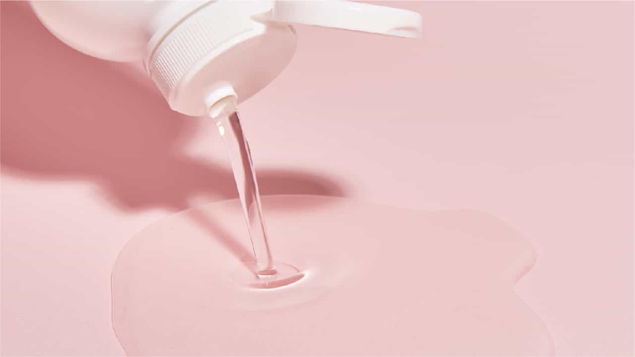 A white bottle pouring a puddle of unflavored MCT oil onto a pink surface.