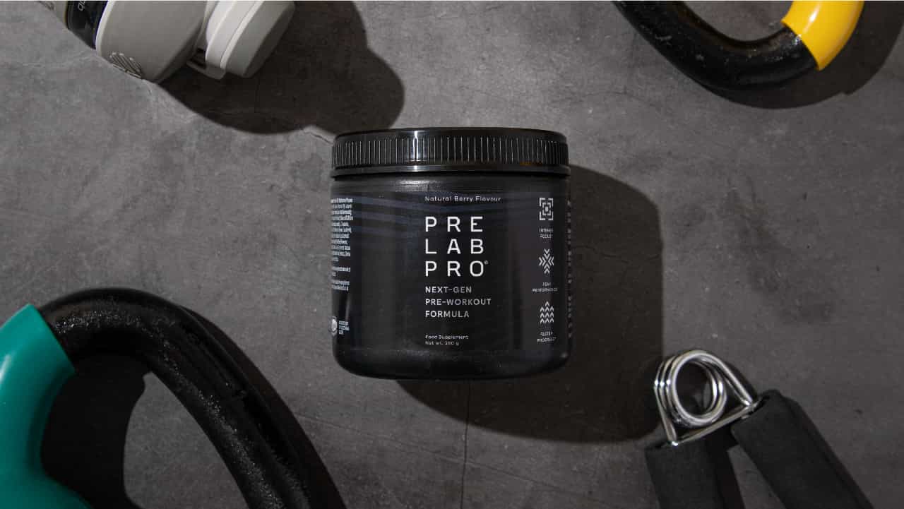 Pre Lab Pro bottle sitting label-up on a gritty gym floor surrounded by workout gear. A top pre-workout supplement for women to intensify arm workouts.