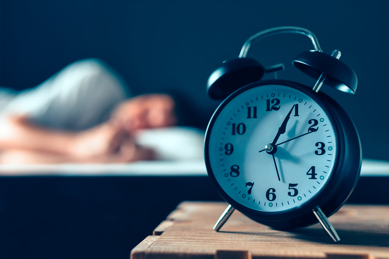 Man sleeping in a dark bedroom with a clock showing after use of Magnesium for sleep