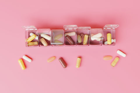 Clear pill box with 7 compartments holding various capsules on a pink background.