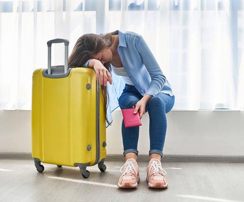 Woman in airport leaning on a yellow suitcase looking exhausted.