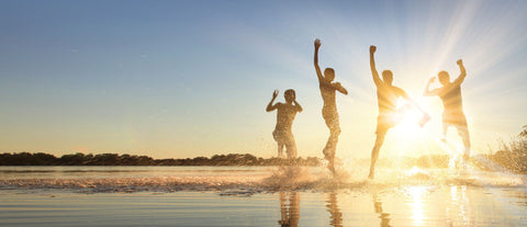 4 people on a beach at the sea's edge silhouetted by the sun, splashing and having fun.