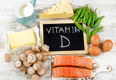 A chalkboard with 'Vitamin D' written on it surrounded by foods that contain vitamin D such as salmon, mushrooms, cheese and milk.