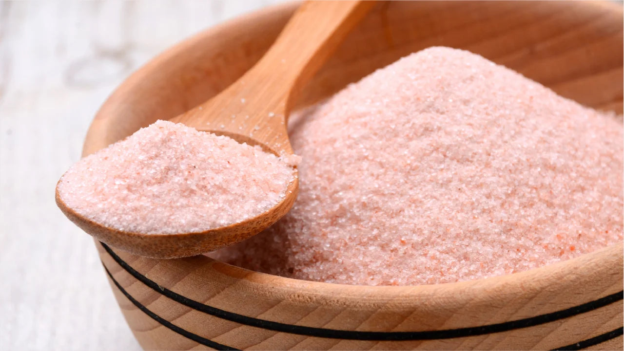 A wooden bowl of himalayan pink salt with a full spoon of salt perched on top. Himalayan pink salt naturally supplies electrolytes.