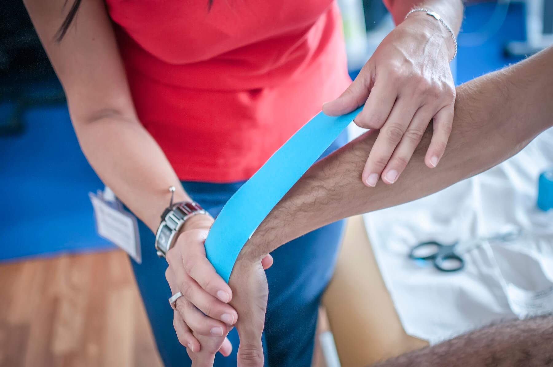 Applying kinesiology tape on forearm for injury support.