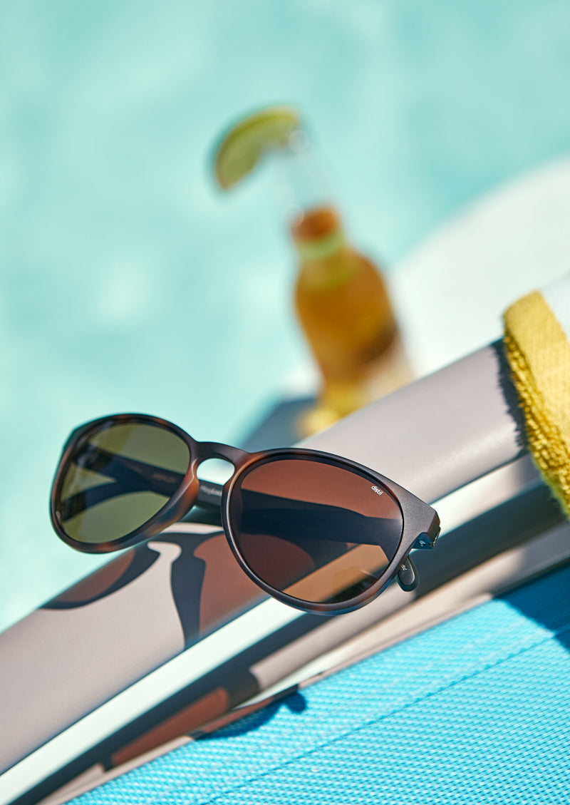A pair of MagLock sunglasses attached to a magnetic chair beside a pool