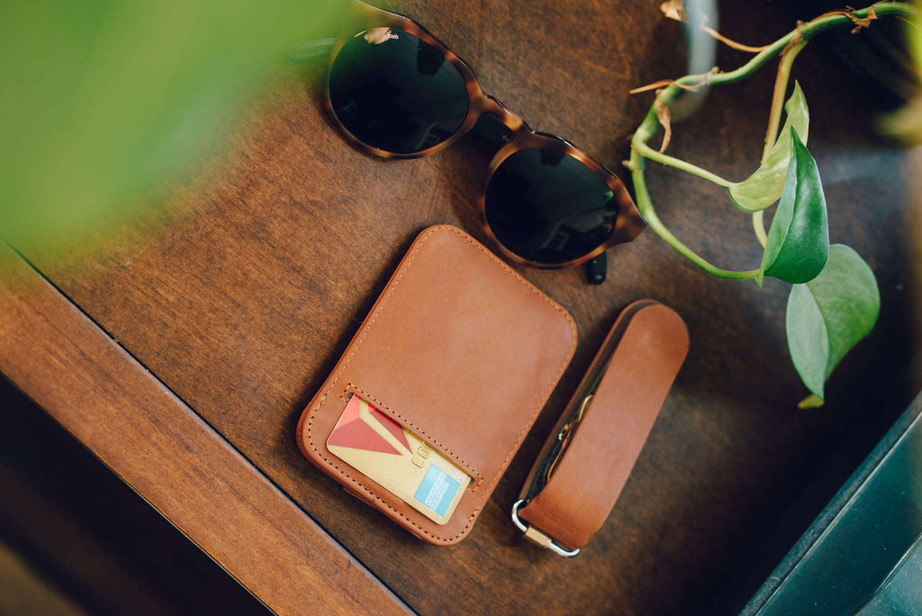 cooper sunglasses, wally sleeve, and keyloop kit by distil union rests on a wooden bench