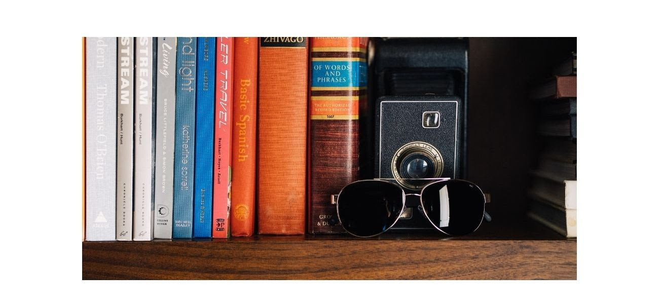A pair of Distil Union MagLock sunglasses sit on a bookshelf with a vintage camera