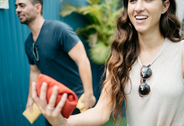 A man and woman smile as they play cornhole outside, both have a pair of Distil Union MagLock Sunglasses clipped to their shirts