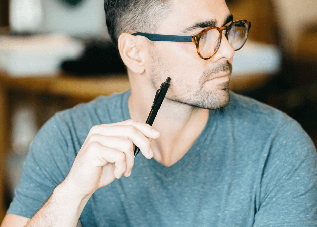 man with glasses holding pen and thinking
