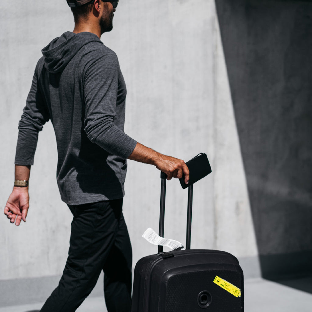 A man carries a Distil Union Passport Cover+ while at the airport with his rolling luggage