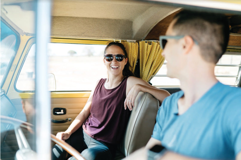 A smiling woman wearing MagLock Sunglasses sits in a VW van with a guy smiling at her