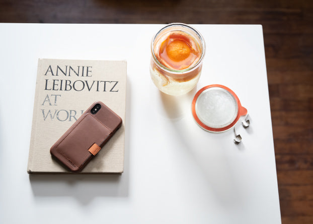 A brown leather Wally Case sits on top of an Annie Leibovitz book with a jar of water with orange in it