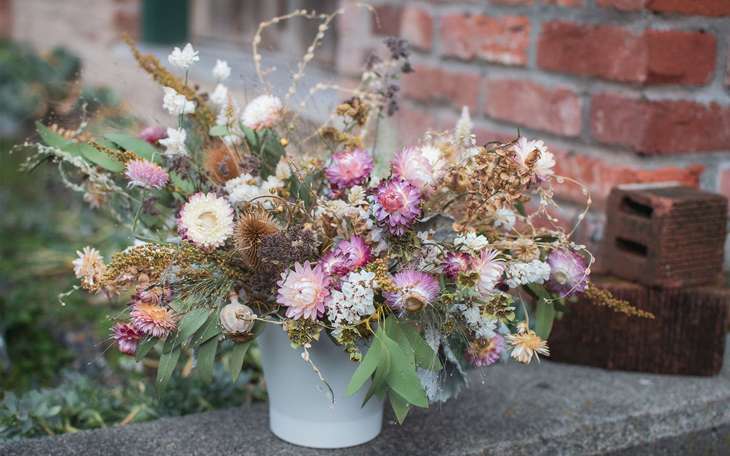 A dried flower centerpiece full of love light pinks and neutral preserved flowers in a white pot.