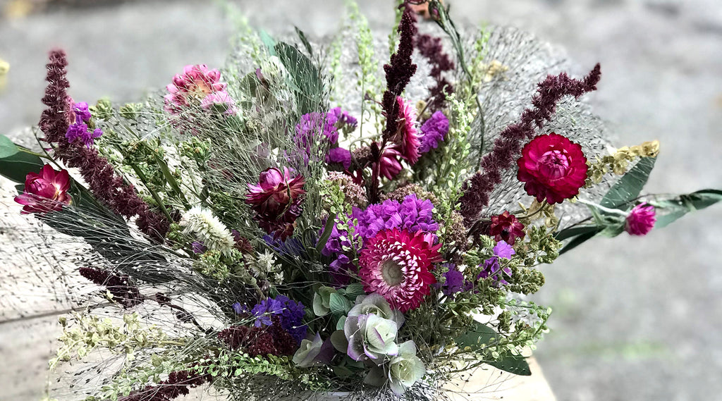 Dried flower arrangement with pink and purple strawflower, amaranth, statice, cress, and seed pods.