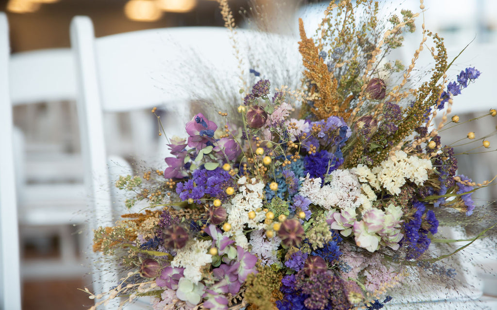 Dried flower wedding bouquet with purples, blues, gold, and white flowers.