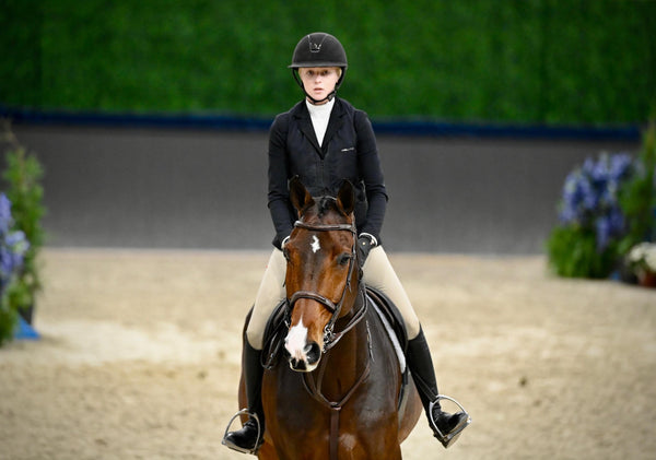 Carlee cantering towards the camera on her horse, looking towards a jump with their game faces on.