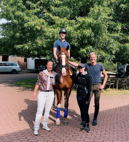 Hope Cooper standing with two trainers next to a trainer on top of a horse smiling at camera.