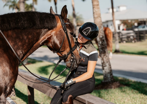 Hope sitting on a fence with her horse, smiling and petting his face.