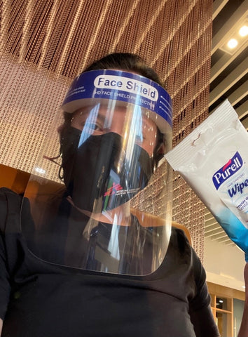 Hope in an airport holding sanitizing wipes and a mask and face shield on her face.