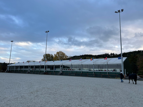 Horse arena with white tents along one side and multiple country's flags waving in the wind.