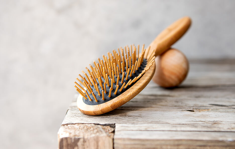 A classic-looking wooden hairbrush balanced on a wooden ball, which are both lay on a rustic table