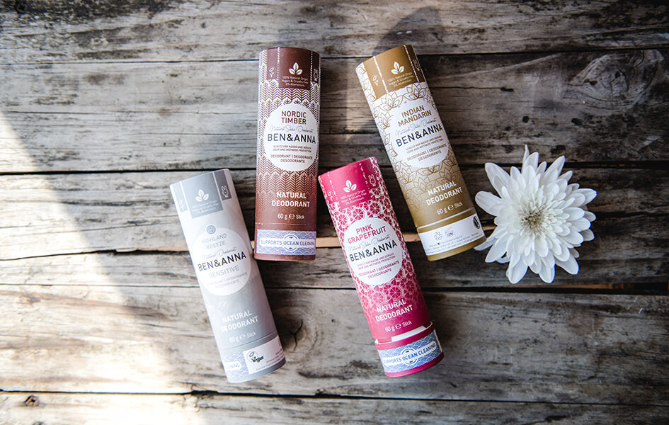 Four colourful plastic-free deodorants on a wooden table with light shining on them