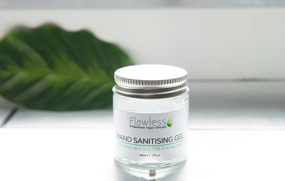 A glass jar of hand sanitiser with aluminium lid. Placed on a windowsill with light coming in from the window and a leaf lay behind the jar