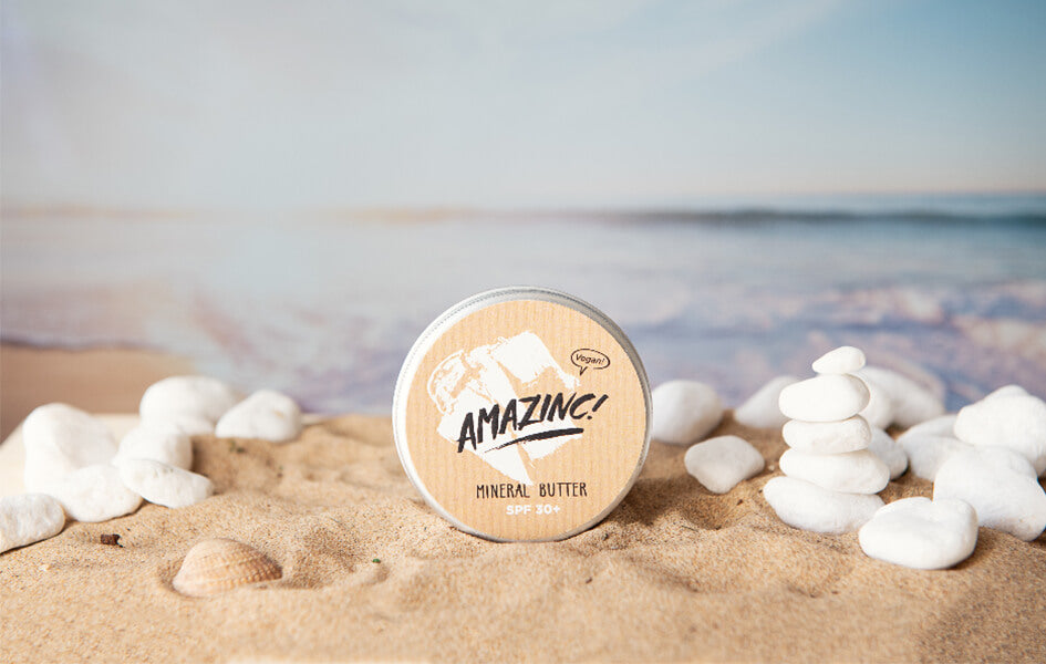 A plastic-free aluminium tin of sun cream on sand surrounded by white pebbles