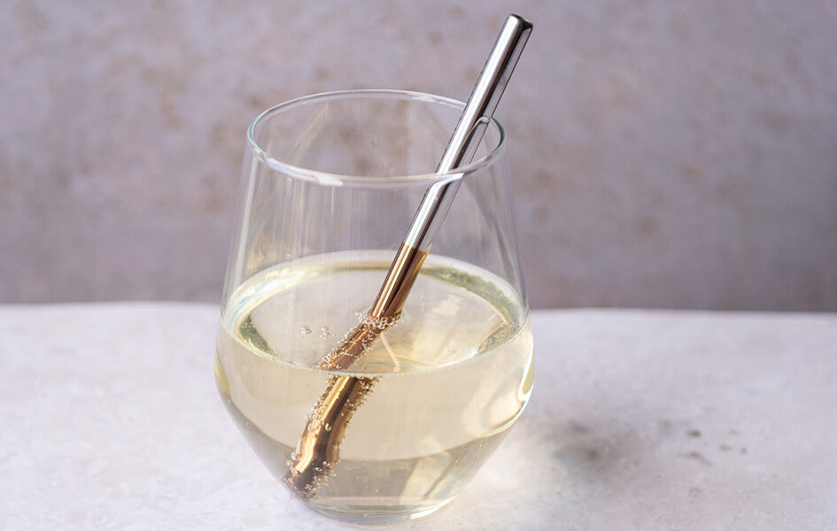 A stylish stainless steel straw in a glass of white sparking wine.