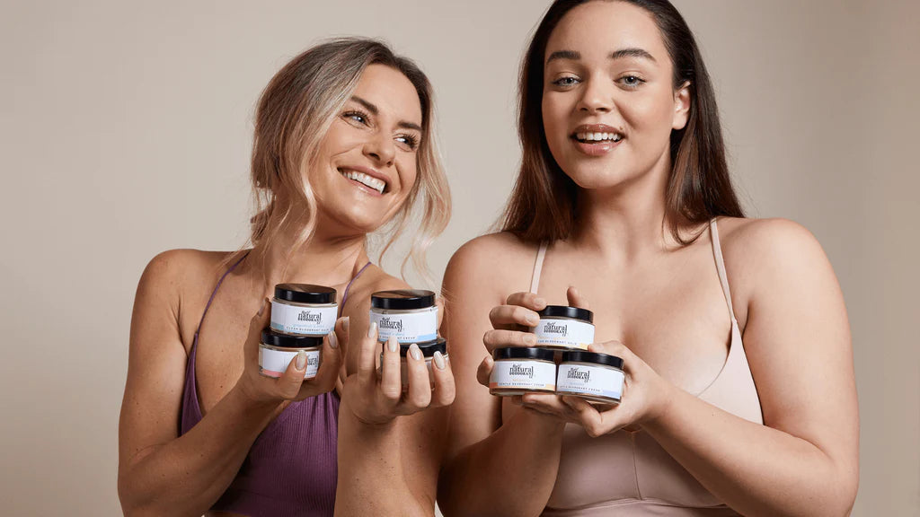 Two women holding various scents and types of Natural Deodorant Company's deodorants