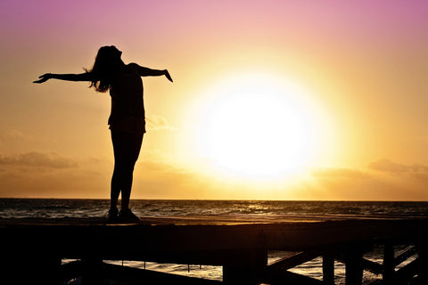 The silhouette of a woman in the sunset spreading her arms in freedom.