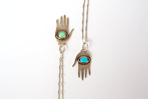 Two silver hand pendants with turquoise eyeballs in the palm on a white background.