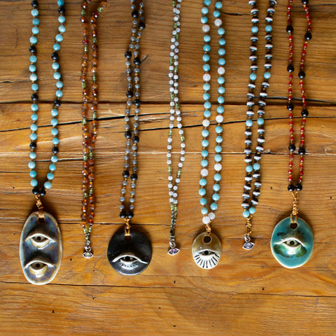 collection of seven beaded necklaces with varying color and pendants on wooden background