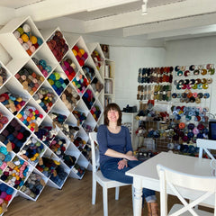 Nicky, owner of All About The Yarn, sitting in front of her diamond shelving full of colourful yarn. Knitting and crochet supplies Chesterblade Hills near Shepton Mallet Somerset