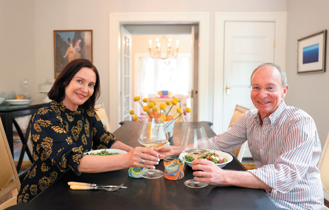 Margaret and her husband Bill sit at their dining room table and cheers with two glasses of wine.