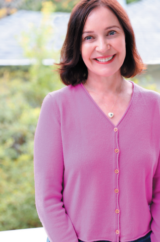 Margaret wearing a bright pink cashmere cardigan and standing in front of her garden.