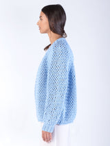 Side view of the model wearing a blue cardigan knit from a large gauge yarn and a off-white dress.