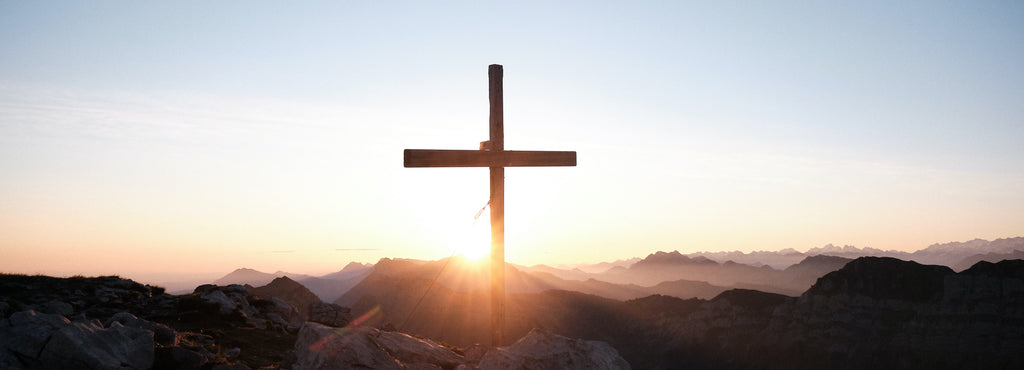 Crucifix in the mountains with the sun rising behind.