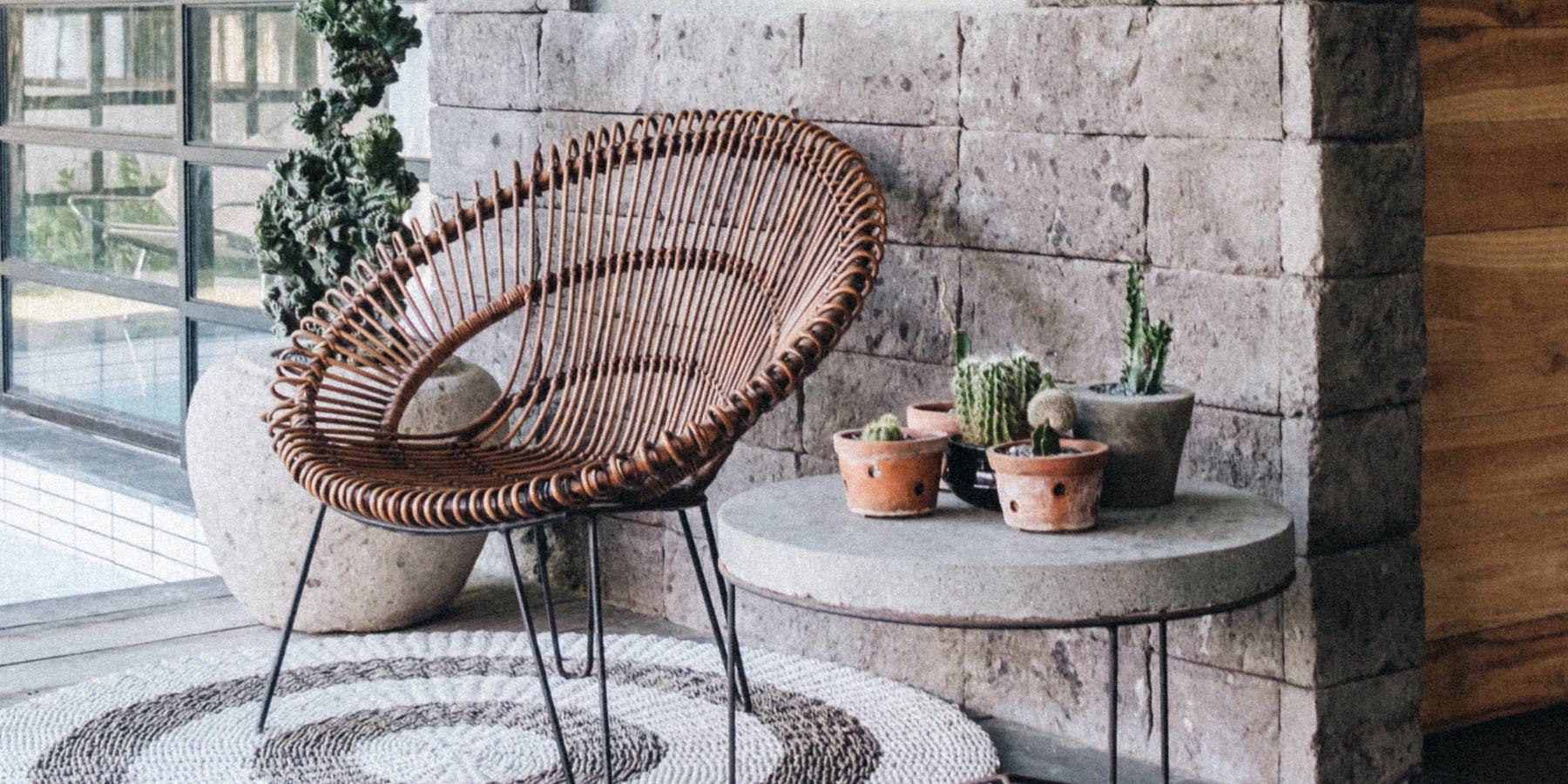 Exterior area featuring a mid-century style chair, a cement exterior coffee table with succulents plant on top. The items are positioned in front a rustic stone wall.