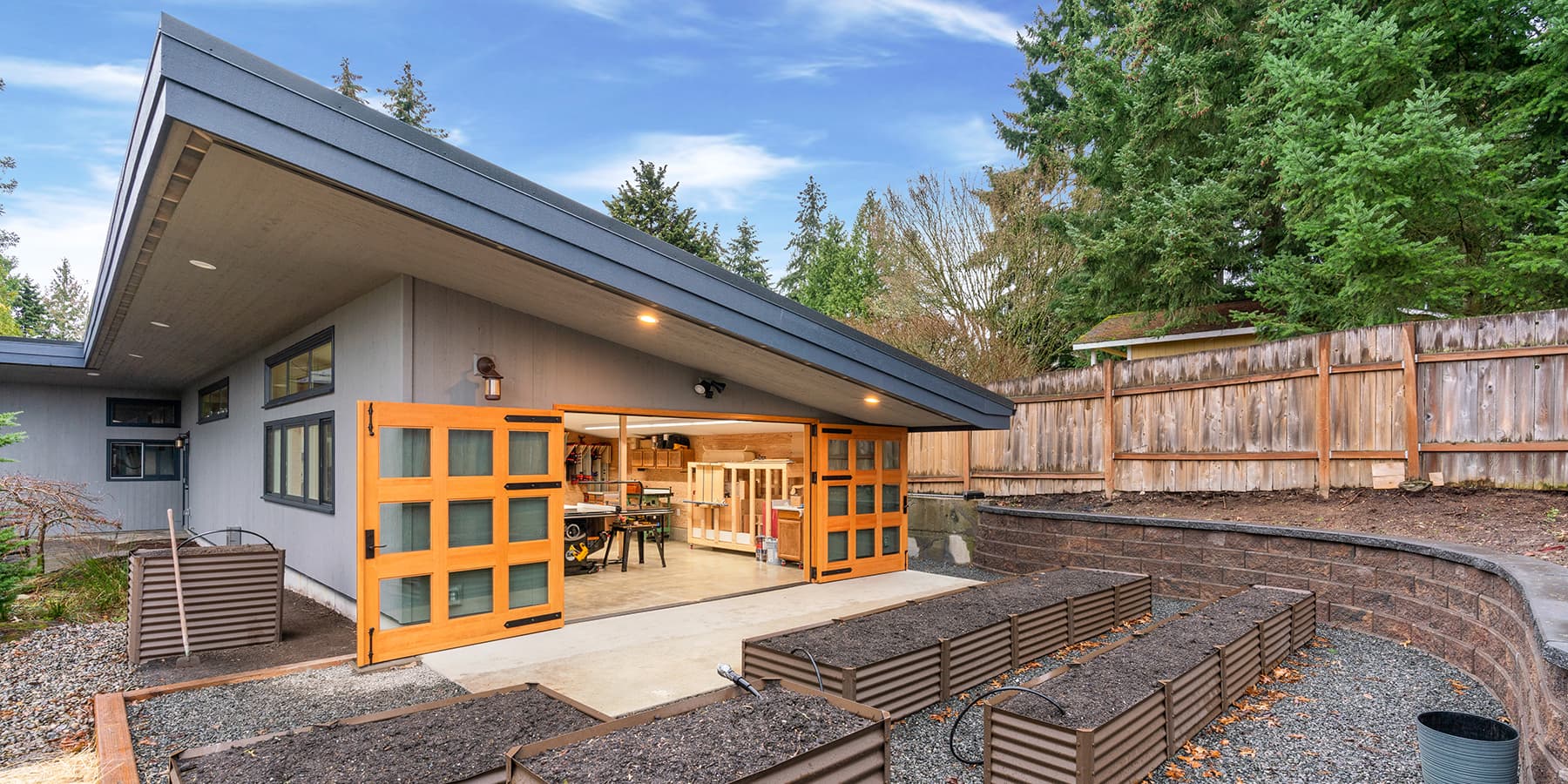 McIntyre Furniture woodshop exterior view. Image highlights set of Vertical Grain Douglas Fir Carriages Doors designed by RealCraft. The carriage doors have 9 individual glass panes on each door and strap hinges were installed for aesthetics.