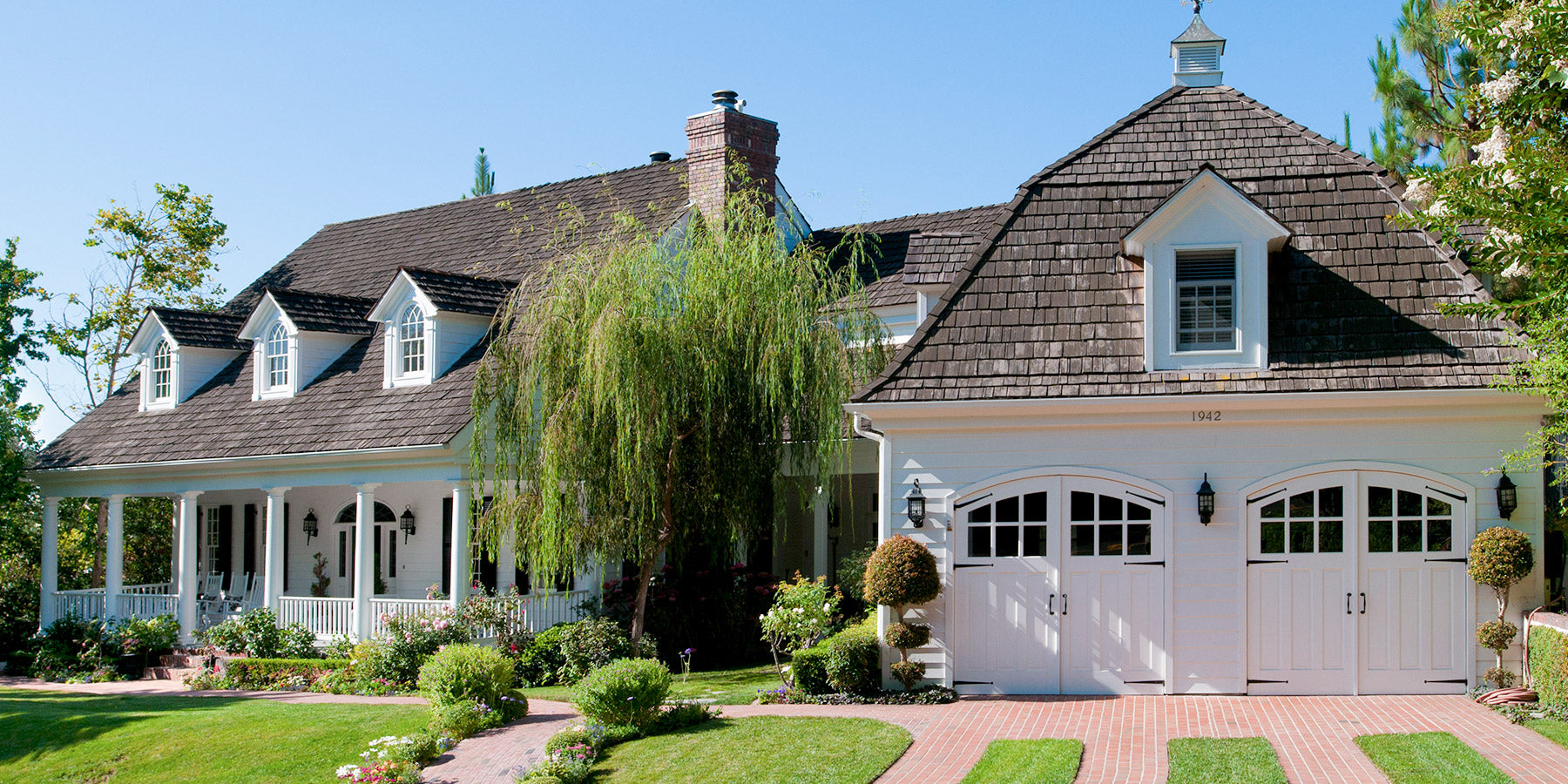 Double set of White Carriage Doors on a traditional home home design in a sunny day. Photo captures the whole house front and garden. Photo by RealCraft.