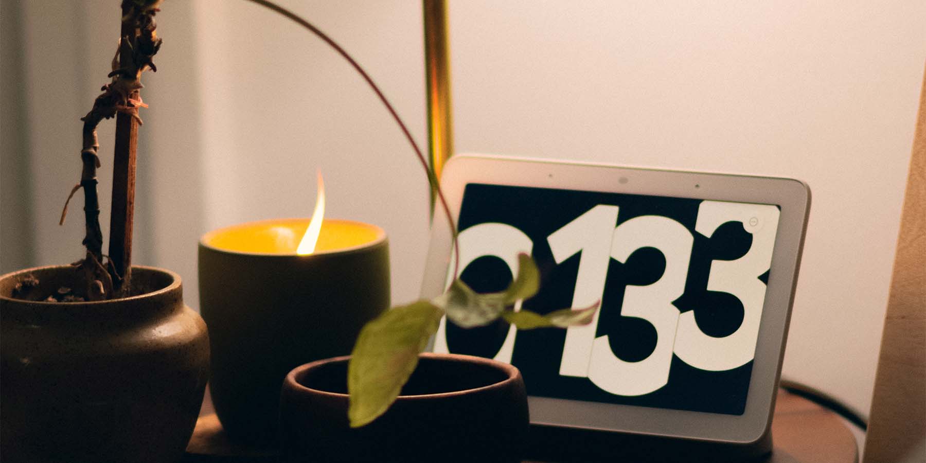 Side table with a plant, a digital clock, and a burning candle.