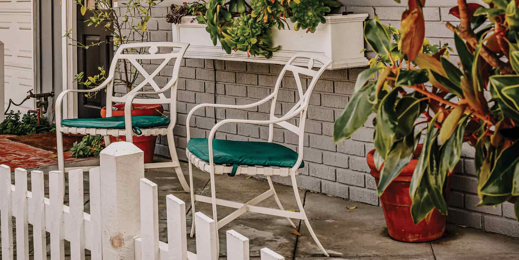 Two white chairs on a patio area with white fence around the porch.