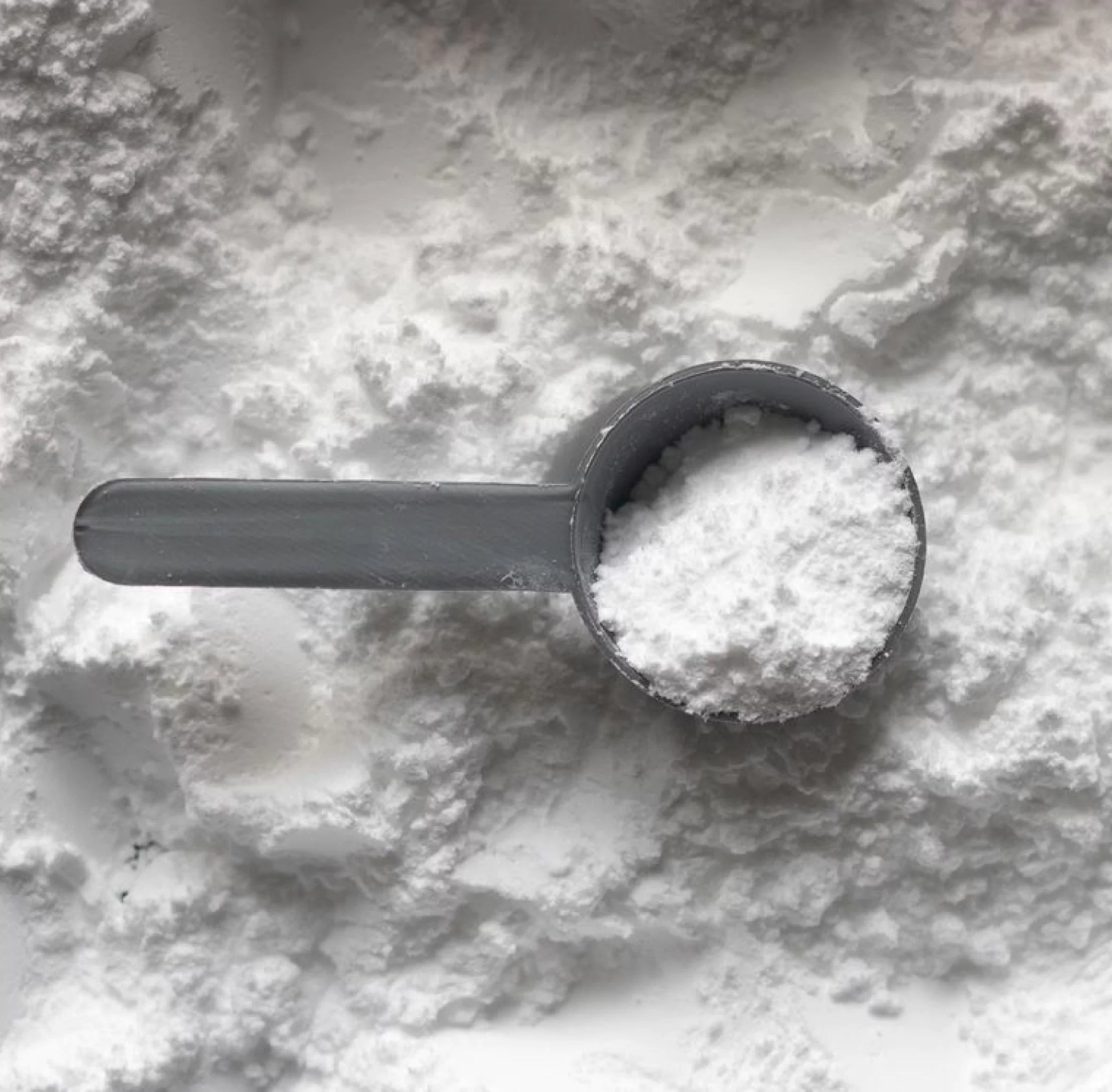 Measuring scoop filled with white powder on a background of scattered white powder.